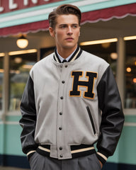 Man wearing a gray and black varsity jacket with a large 'H' on it, standing in front of a building.