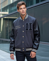 Man wearing a navy varsity jacket with white lettering and accents, standing in front of a modern building.