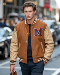 Man wearing a brown and beige varsity jacket with a large 'M' on a city street.