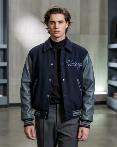 Man wearing a navy and gray varsity jacket with 'Victory' on it in an indoor setting.
